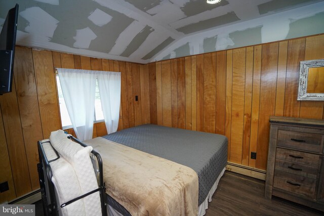 bedroom with a baseboard heating unit, vaulted ceiling, wood walls, and dark wood-type flooring