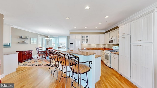 kitchen with a center island with sink, white cabinets, white appliances, and light hardwood / wood-style flooring