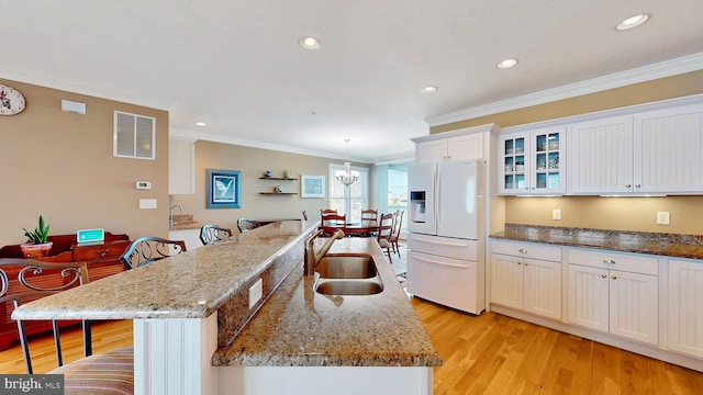 kitchen with a center island with sink, crown molding, white fridge with ice dispenser, and sink