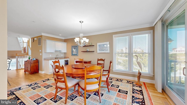 dining room featuring light wood-type flooring, ornamental molding, sink, a notable chandelier, and wine cooler