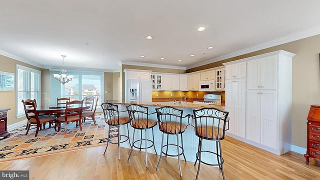 kitchen featuring white appliances, light wood-type flooring, ornamental molding, white cabinetry, and a chandelier