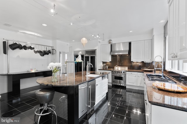 kitchen with a kitchen island with sink, white cabinets, luxury stove, wall chimney range hood, and sink