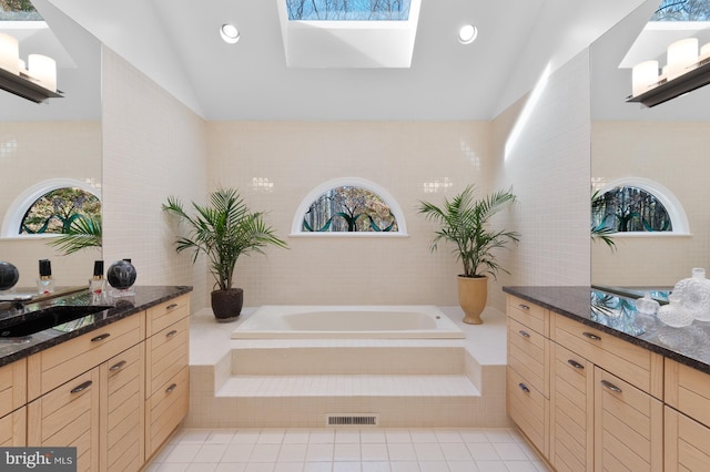 bathroom with a skylight, tile flooring, tiled tub, and vanity