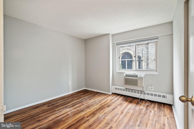 unfurnished room with a baseboard radiator, wood-type flooring, and a wall unit AC