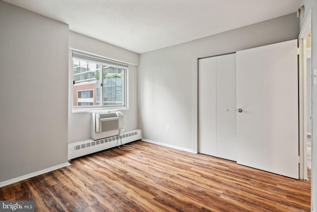 unfurnished bedroom with hardwood / wood-style flooring, an AC wall unit, a baseboard heating unit, and a closet