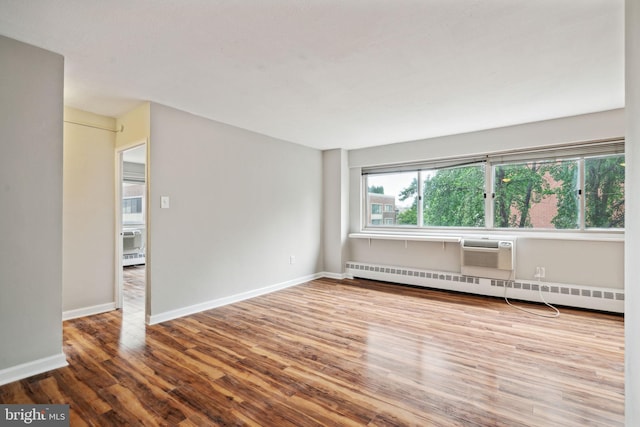 unfurnished room with an AC wall unit, baseboard heating, wood-type flooring, and a healthy amount of sunlight