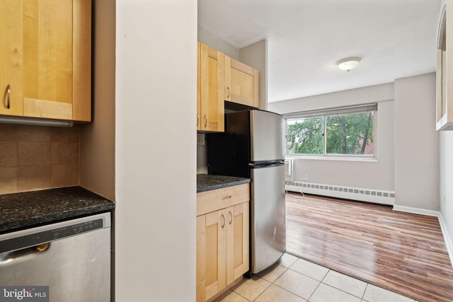 kitchen with appliances with stainless steel finishes, dark stone counters, light tile patterned floors, baseboard heating, and light brown cabinets