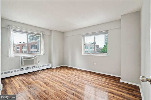 spare room featuring plenty of natural light, a wall mounted air conditioner, wood-type flooring, and a baseboard heating unit