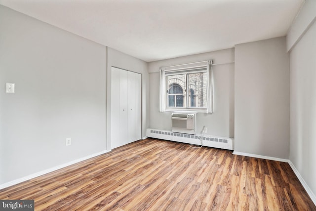 empty room with a wall mounted air conditioner, hardwood / wood-style floors, and baseboard heating