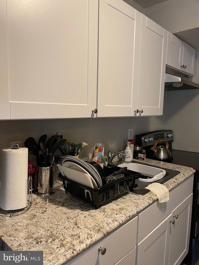 kitchen featuring light stone countertops, white cabinetry, and range