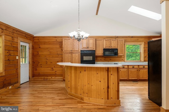 kitchen featuring lofted ceiling with skylight, wood walls, black appliances, and decorative light fixtures