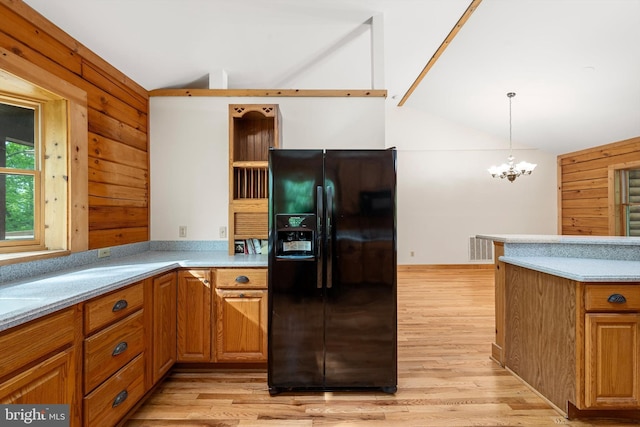 kitchen with pendant lighting, wood walls, black fridge, light hardwood / wood-style flooring, and a notable chandelier