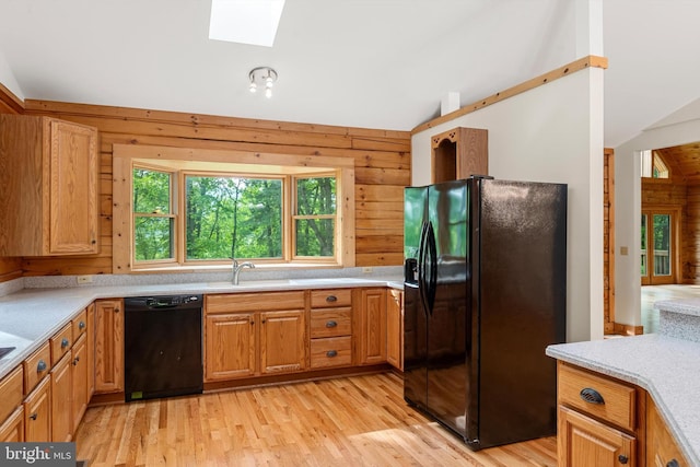 kitchen with black appliances, sink, wooden walls, vaulted ceiling with skylight, and light wood-type flooring