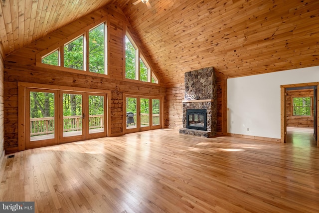 unfurnished living room featuring high vaulted ceiling, a stone fireplace, ceiling fan, light hardwood / wood-style floors, and wood ceiling