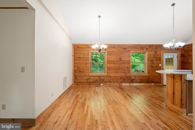 unfurnished dining area with light hardwood / wood-style floors, a notable chandelier, and wood walls