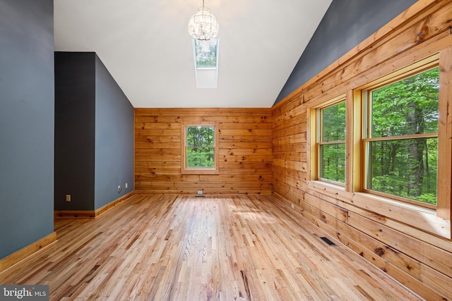 additional living space featuring wooden walls, a notable chandelier, lofted ceiling with skylight, and light wood-type flooring