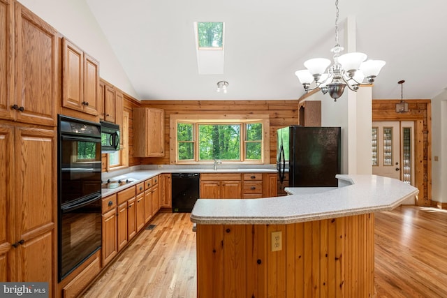 kitchen with lofted ceiling with skylight, black appliances, hanging light fixtures, light wood-type flooring, and a notable chandelier