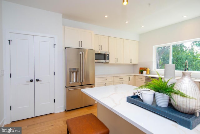 kitchen with light hardwood / wood-style floors, appliances with stainless steel finishes, decorative backsplash, light stone countertops, and white cabinets