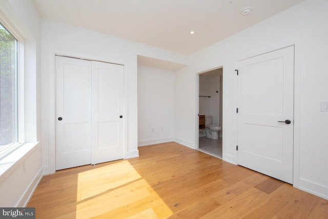 unfurnished bedroom with a closet, ensuite bath, and light wood-type flooring