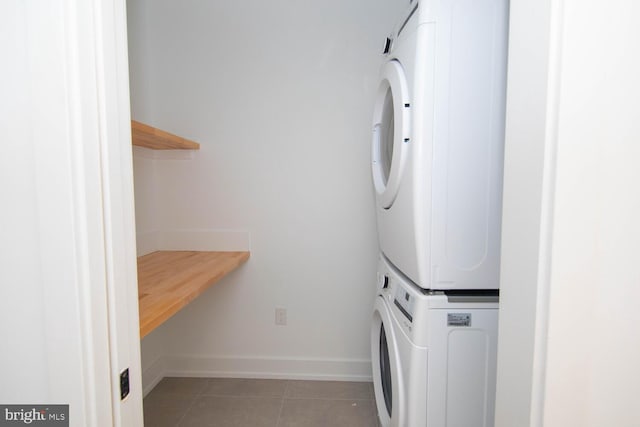 clothes washing area with dark tile patterned floors and stacked washer and clothes dryer