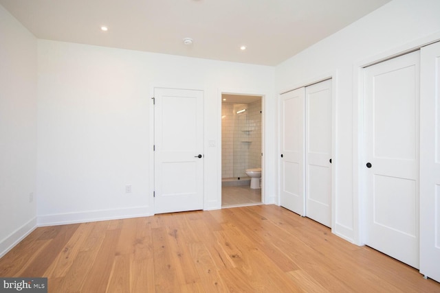 unfurnished bedroom with ensuite bath, light wood-type flooring, and multiple closets