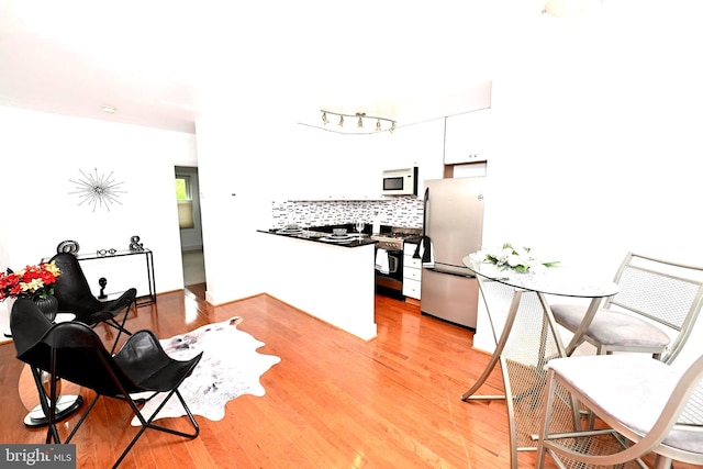 kitchen with stainless steel refrigerator, white cabinets, backsplash, and light wood-type flooring