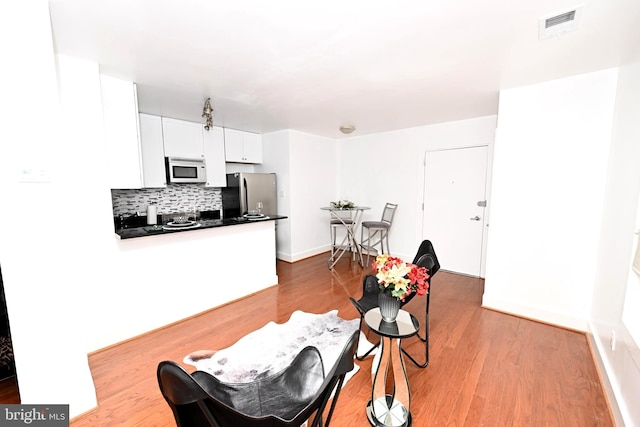 interior space featuring kitchen peninsula, light hardwood / wood-style floors, tasteful backsplash, stainless steel refrigerator, and white cabinetry