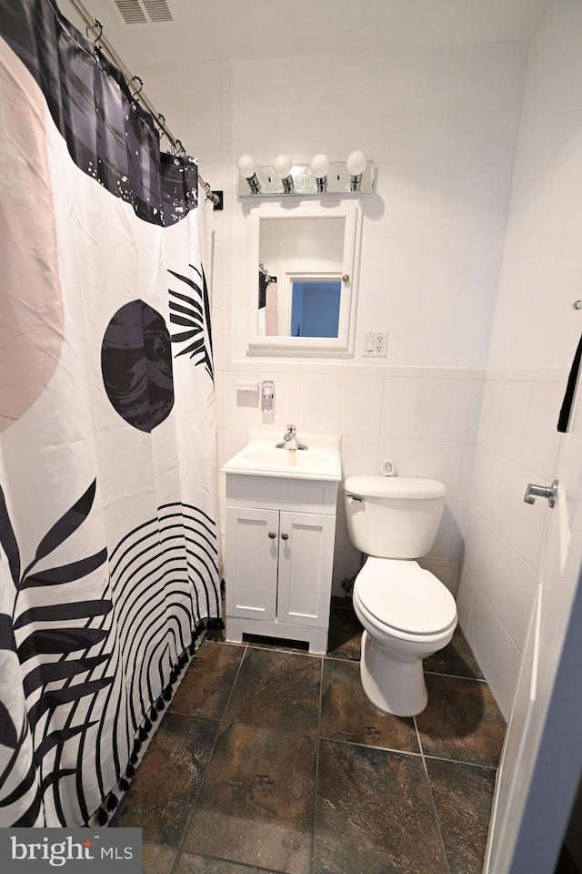 bathroom with vanity, toilet, tile flooring, and tile walls