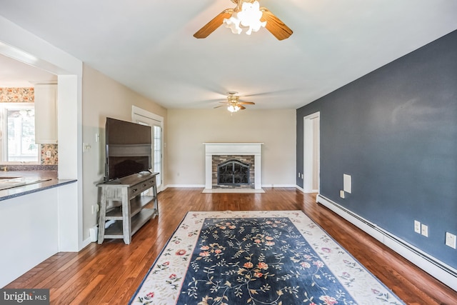 living room featuring a stone fireplace, dark hardwood / wood-style flooring, ceiling fan, and a baseboard heating unit