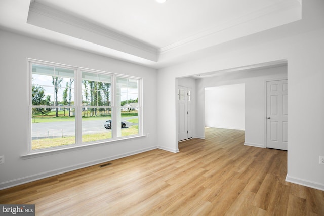 spare room featuring a tray ceiling, crown molding, light wood-style floors, and visible vents