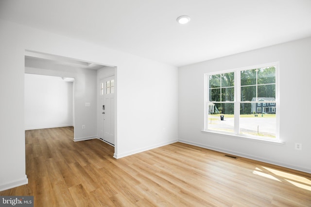 empty room with light wood finished floors, visible vents, and baseboards