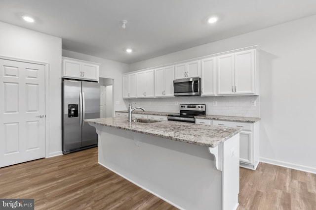 kitchen with a sink, light wood-style flooring, appliances with stainless steel finishes, white cabinets, and a kitchen island with sink