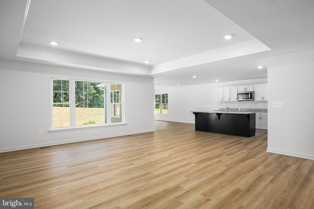 unfurnished living room featuring light wood-style flooring, crown molding, and a raised ceiling