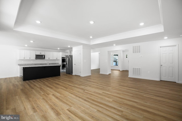 unfurnished living room featuring a tray ceiling, crown molding, and visible vents