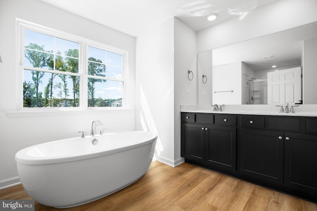 full bathroom with a stall shower, a sink, wood finished floors, double vanity, and a freestanding bath