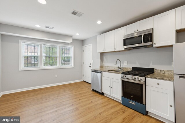 kitchen featuring sink, appliances with stainless steel finishes, dark stone countertops, white cabinetry, and light hardwood / wood-style floors