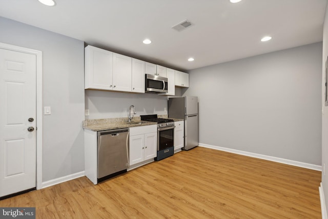 kitchen with appliances with stainless steel finishes, light stone counters, white cabinets, and light wood-type flooring