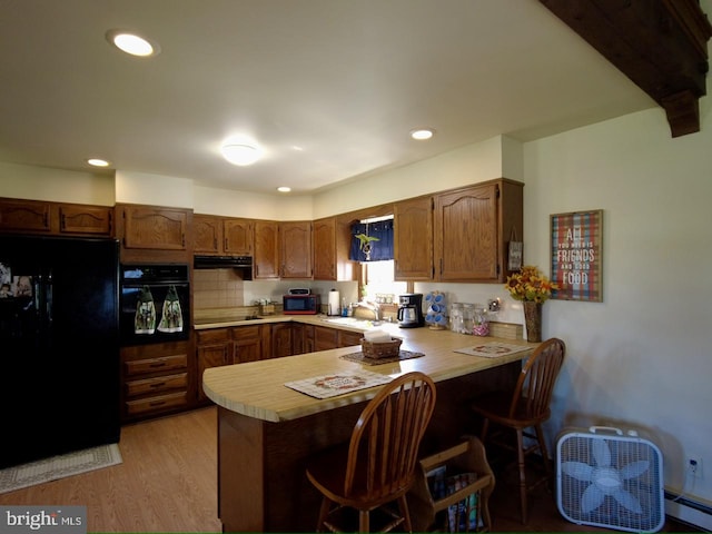 kitchen featuring black appliances, sink, light hardwood / wood-style flooring, kitchen peninsula, and a breakfast bar area