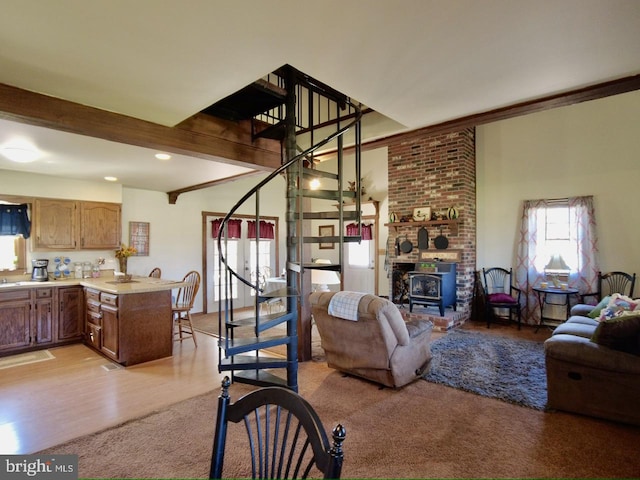 living room featuring beam ceiling, light wood-type flooring, a wood stove, and ornamental molding