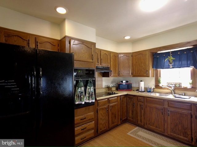 kitchen with light wood-type flooring, sink, tasteful backsplash, and black appliances