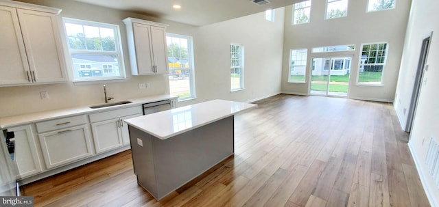 kitchen with white cabinets, dishwasher, a center island, sink, and light hardwood / wood-style flooring