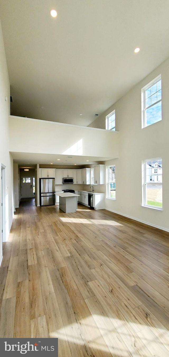 unfurnished living room with a towering ceiling and light wood-type flooring