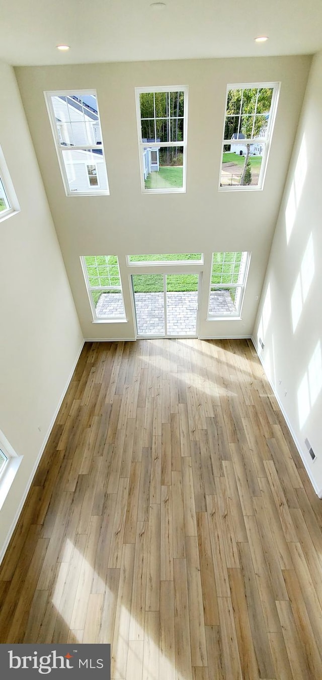 unfurnished living room with a high ceiling, plenty of natural light, and light wood-type flooring