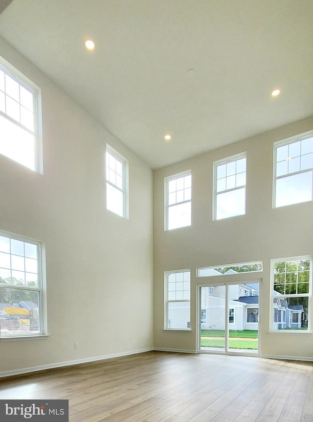 unfurnished living room featuring light wood-type flooring and a towering ceiling