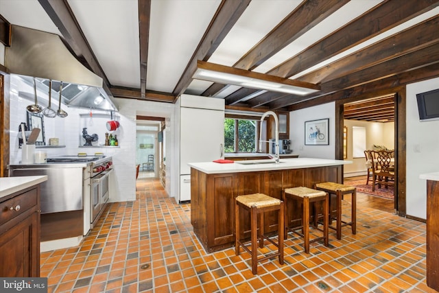 kitchen featuring a breakfast bar, sink, beam ceiling, a center island with sink, and double oven range