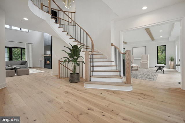 foyer featuring recessed lighting, light wood-style flooring, a high ceiling, a glass covered fireplace, and stairs