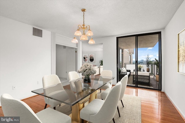 dining space featuring expansive windows, light hardwood / wood-style floors, a textured ceiling, and an inviting chandelier