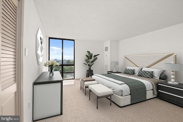 bedroom with light colored carpet, a textured ceiling, and a wall of windows