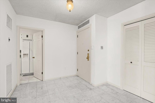 unfurnished bedroom featuring white refrigerator with ice dispenser, a textured ceiling, and a closet