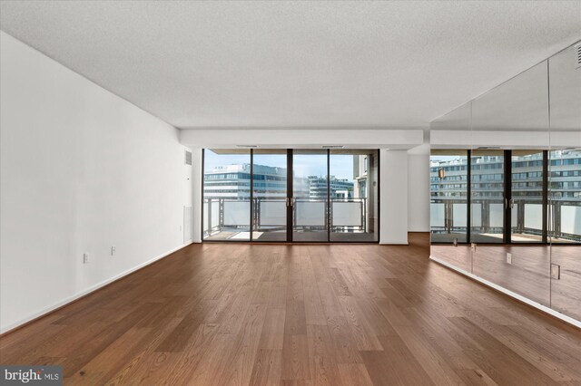 unfurnished room with floor to ceiling windows, a textured ceiling, hardwood / wood-style flooring, and plenty of natural light